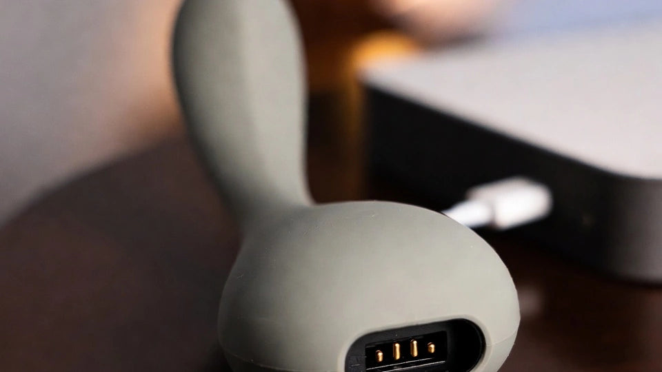 A dry rechargeable silicone wellness device resting beside its charging cable, highlighting careful charging-port and