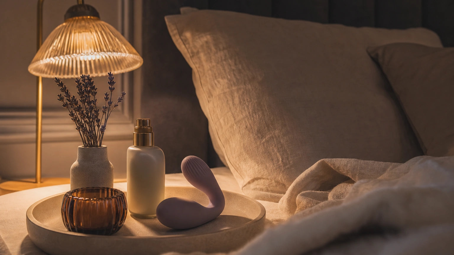 Minimalist bedside setup with linen bedding, warm lamp, moisturizer, ceramic tray, and sculptural silicone massager